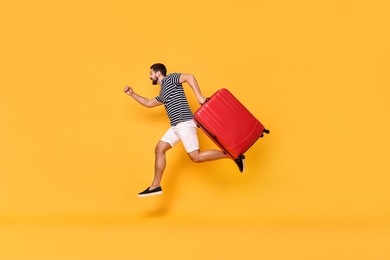 Photo of Happy man with suitcase running on orange background