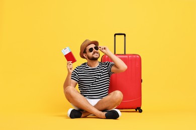 Photo of Happy man in sunglasses with passport, tickets and suitcase on orange background