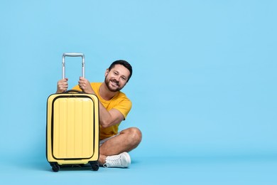 Photo of Happy man with suitcase on light blue background, space for text