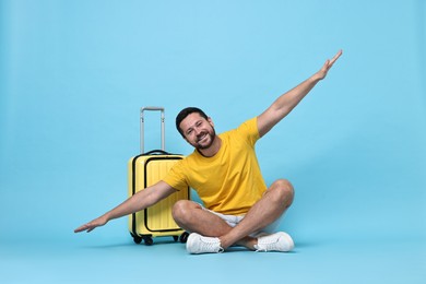 Photo of Happy man with suitcase on light blue background