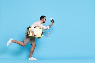 Photo of Happy man in sunglasses with suitcase on light blue background, space for text