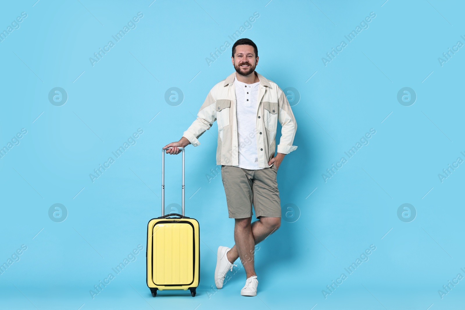 Photo of Happy man with suitcase on light blue background