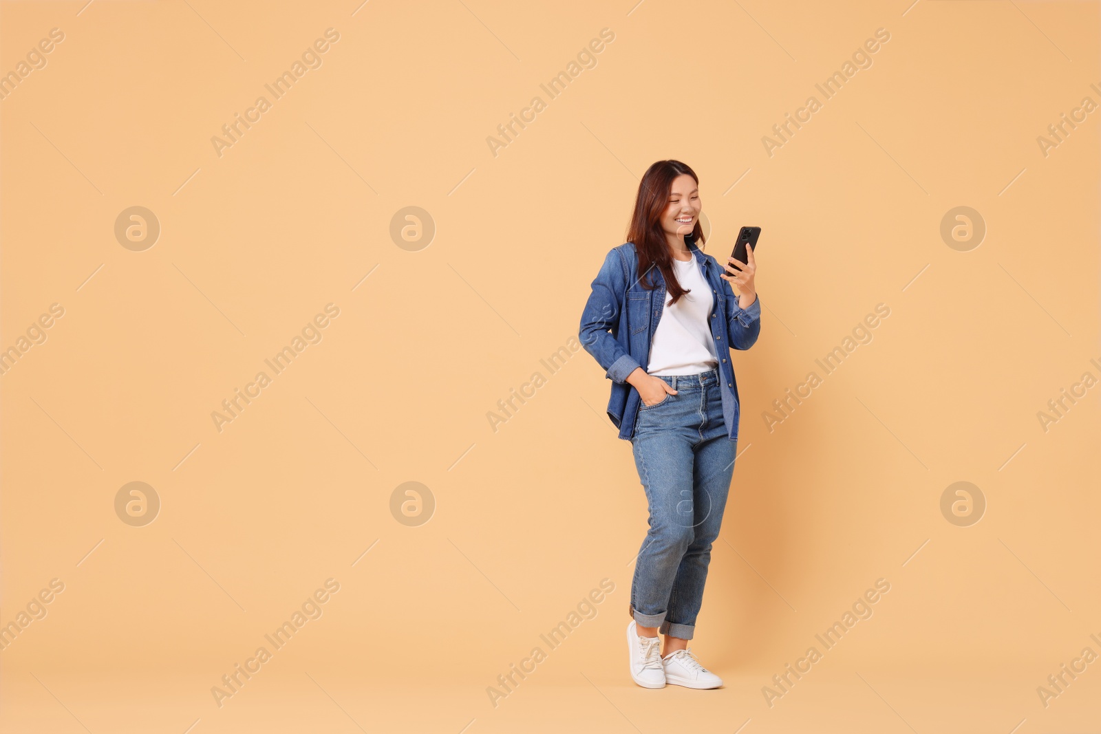 Photo of Smiling woman using smartphone on beige background