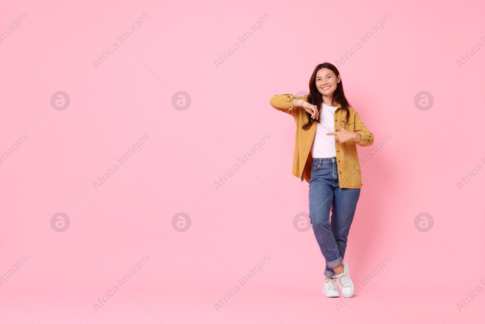 Photo of Smiling woman pointing at something on pink background. Space for text