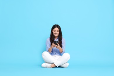 Photo of Smiling woman using smartphone on light blue background