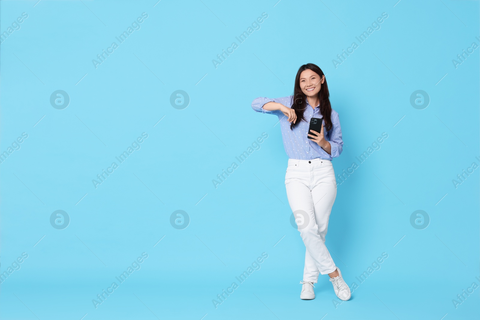 Photo of Smiling woman with smartphone on light blue background. Space for text