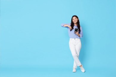 Photo of Smiling woman with smartphone on light blue background. Space for text