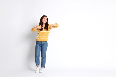 Photo of Smiling woman pointing at something on white background. Space for text