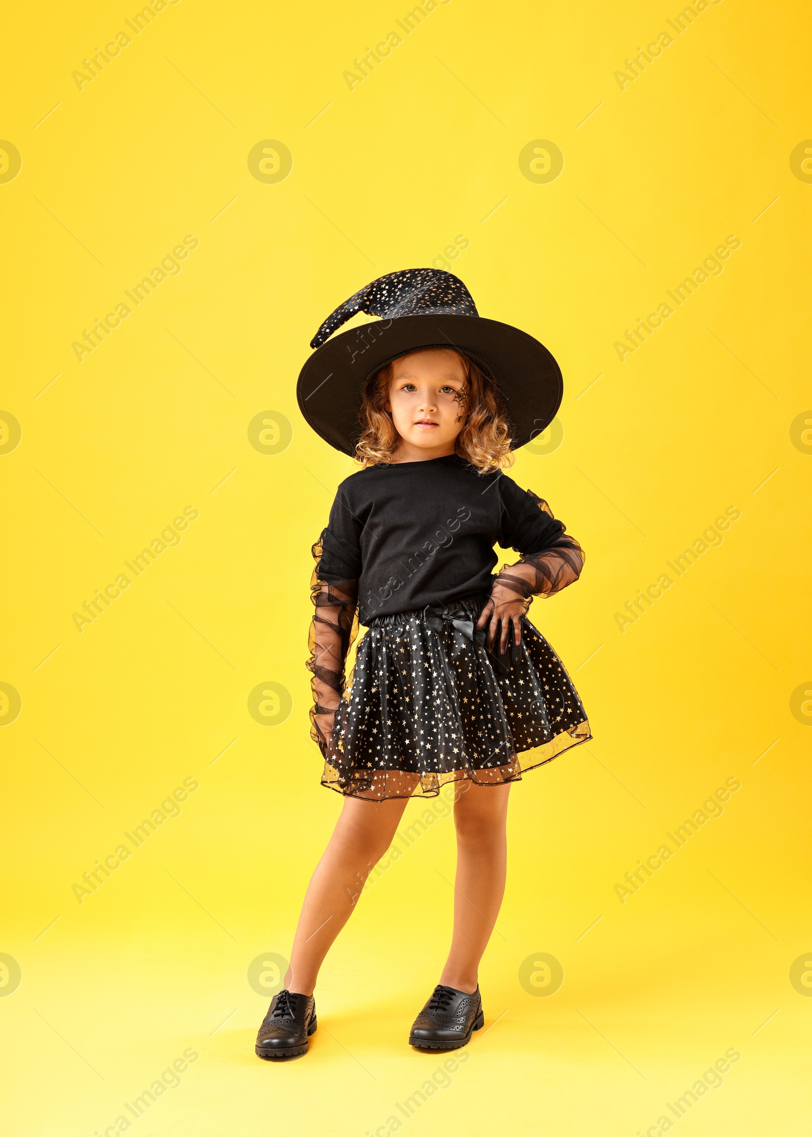 Photo of Cute girl dressed like witch on yellow background. Halloween costume