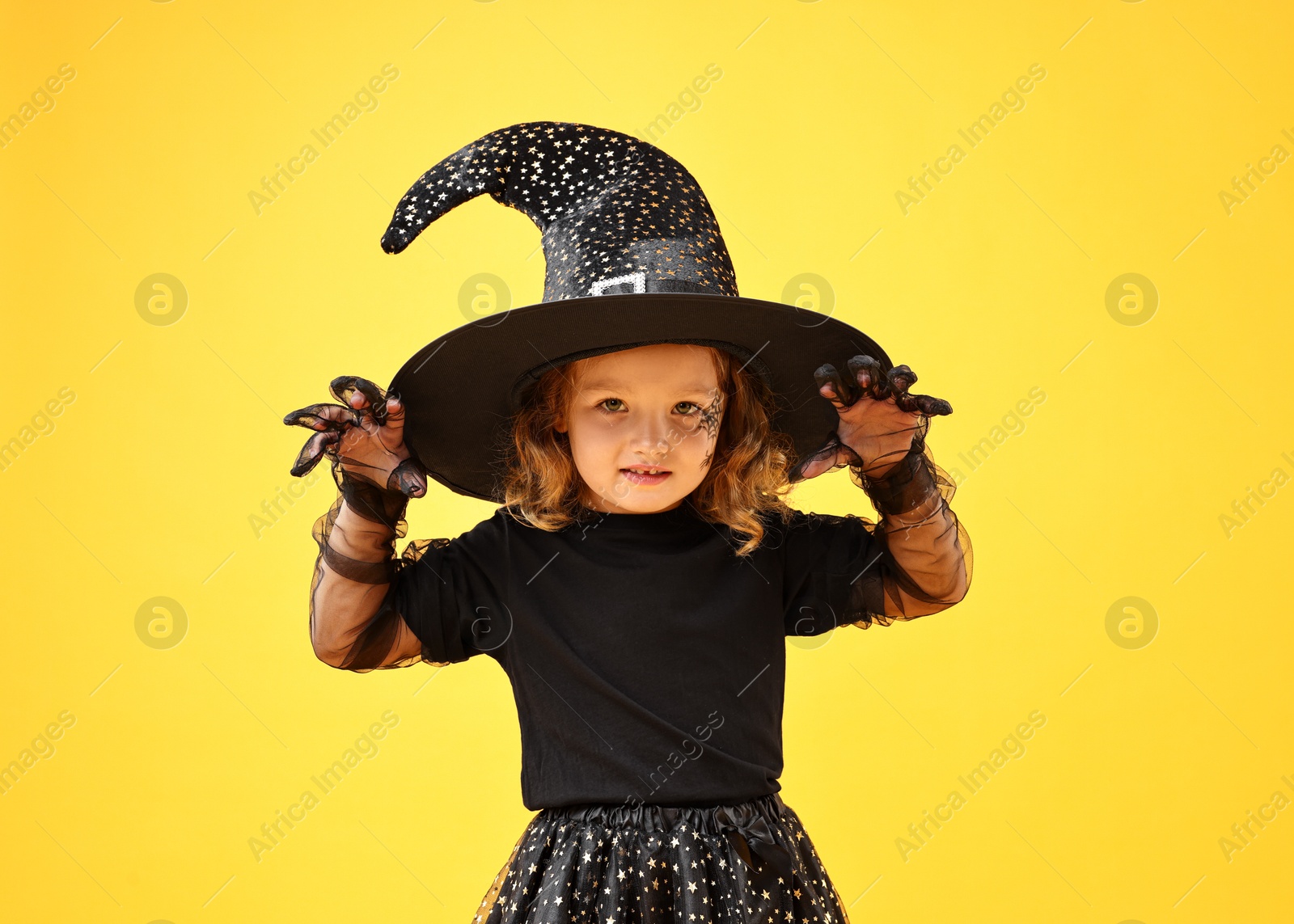 Photo of Cute girl dressed like witch on yellow background. Halloween costume