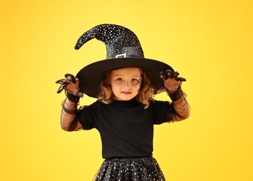 Cute girl dressed like witch on yellow background. Halloween costume