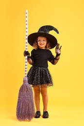 Photo of Cute girl with broom dressed like witch on yellow background. Halloween celebration