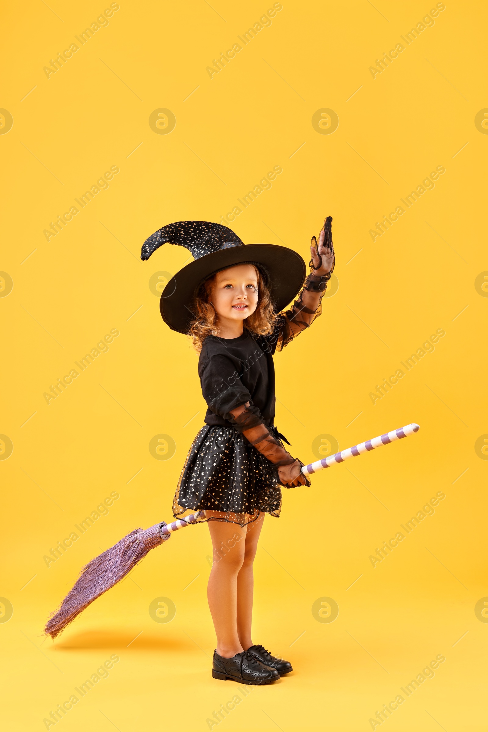 Photo of Cute girl with broom dressed like witch on yellow background. Halloween celebration