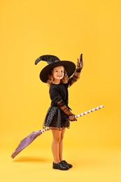 Cute girl with broom dressed like witch on yellow background. Halloween celebration