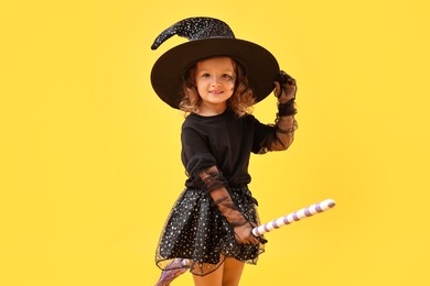 Photo of Cute girl with broom dressed like witch on yellow background. Halloween celebration