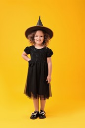 Cute girl dressed like witch on yellow background. Halloween costume