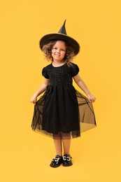 Cute girl dressed like witch on yellow background. Halloween costume