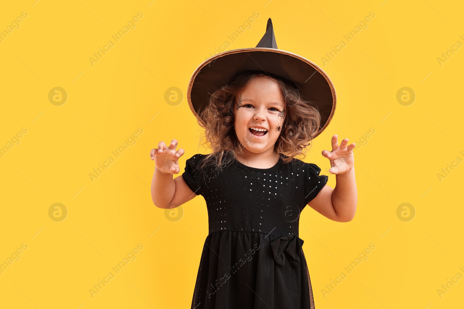 Photo of Cute girl dressed like witch on yellow background. Halloween costume