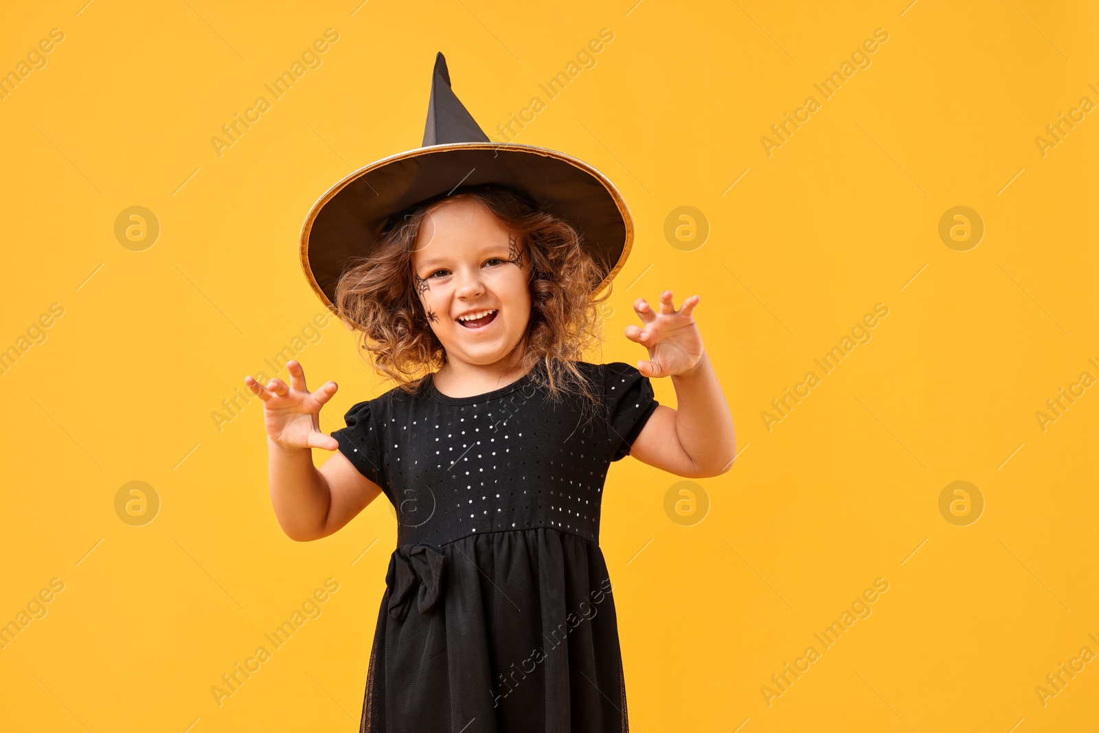 Photo of Cute girl dressed like witch on yellow background. Halloween costume