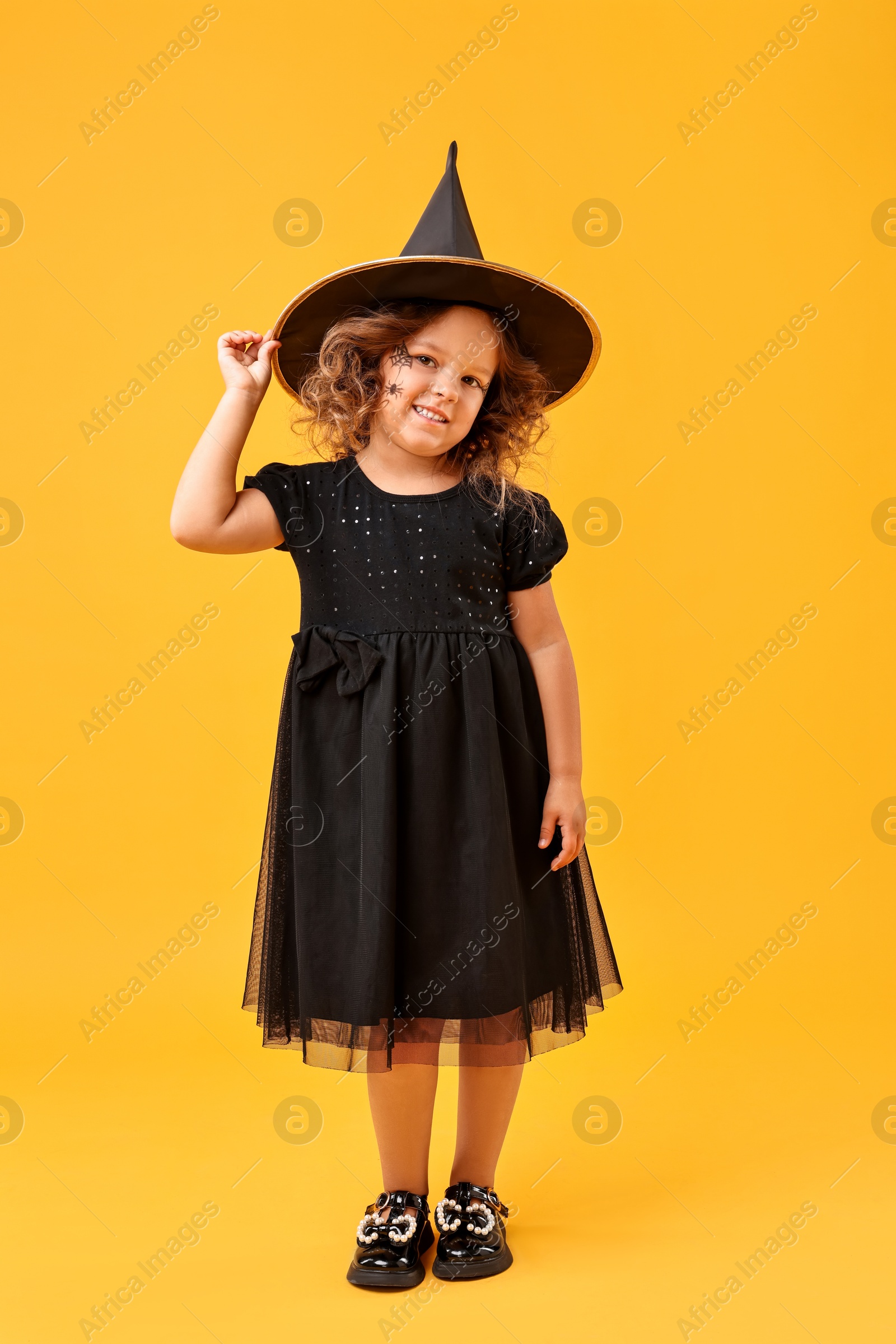 Photo of Cute girl dressed like witch on yellow background. Halloween costume