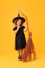 Funny girl with broom dressed like witch on yellow background. Halloween celebration