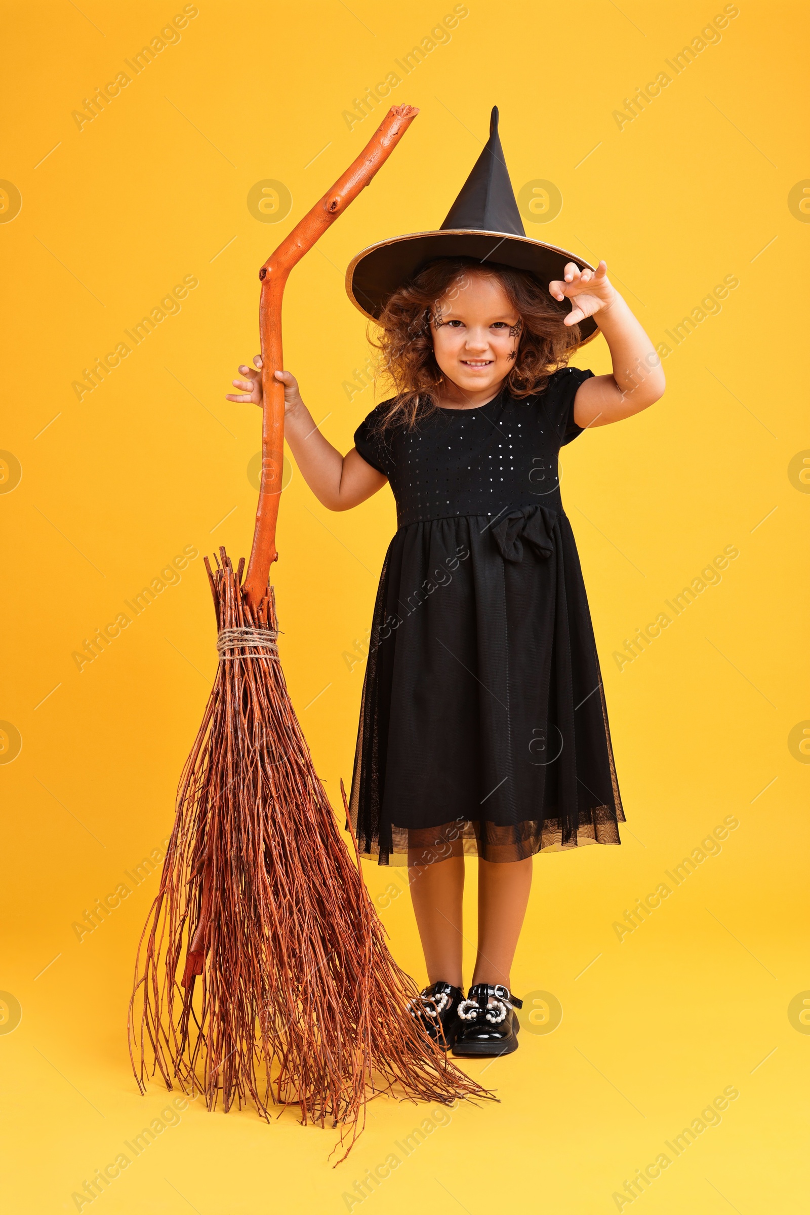 Photo of Funny girl with broom dressed like witch on yellow background. Halloween celebration