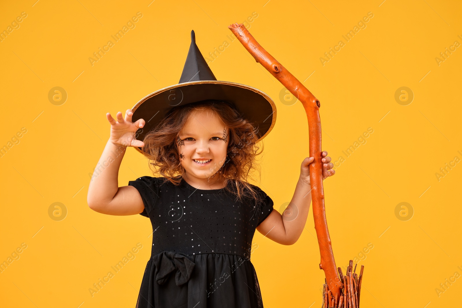 Photo of Funny girl with broom dressed like witch on yellow background. Halloween celebration