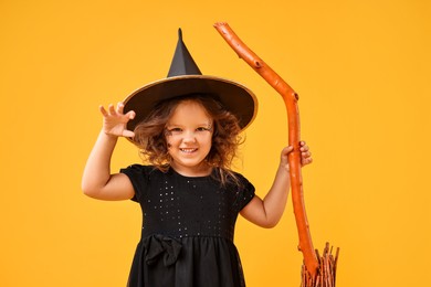 Funny girl with broom dressed like witch on yellow background. Halloween celebration