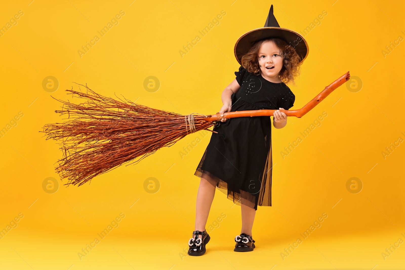 Photo of Funny girl with broom dressed like witch on yellow background. Halloween celebration