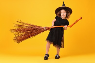 Funny girl with broom dressed like witch on yellow background. Halloween celebration