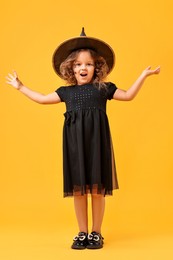 Cute girl dressed like witch on yellow background. Halloween costume