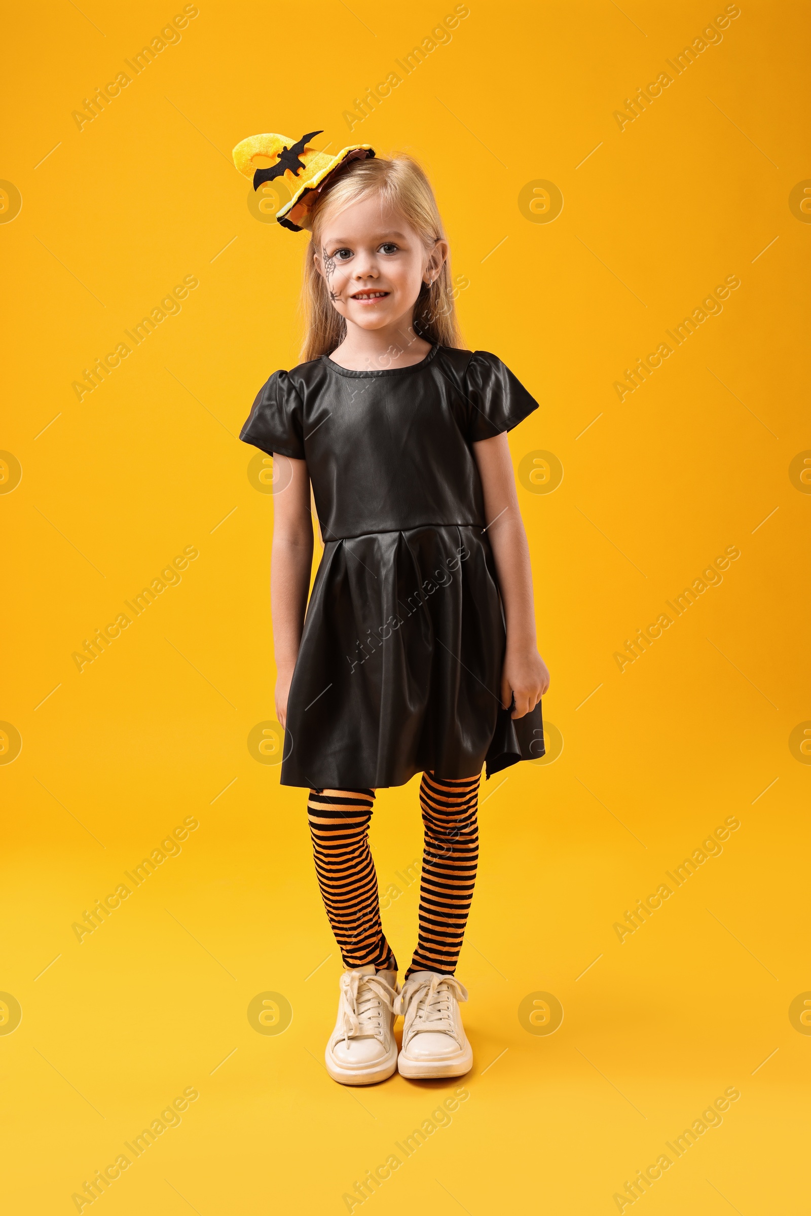 Photo of Cute girl dressed like witch on yellow background. Halloween celebration