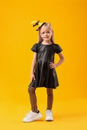 Cute girl dressed like witch on yellow background. Halloween celebration