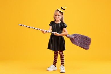 Funny girl with broom dressed like witch on yellow background. Halloween celebration