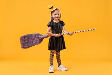 Photo of Funny girl with broom dressed like witch on yellow background. Halloween celebration