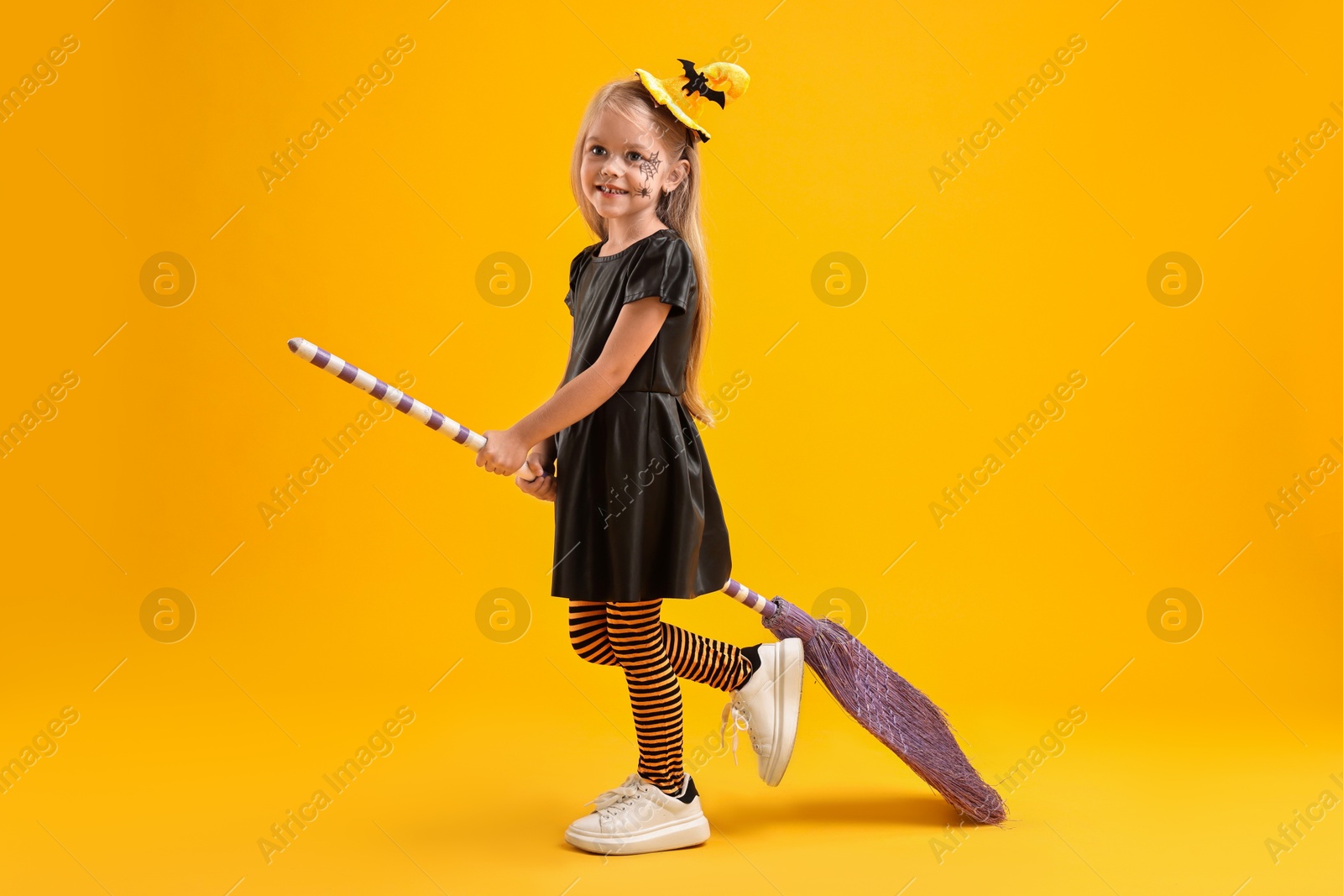 Photo of Funny girl with broom dressed like witch on yellow background. Halloween celebration