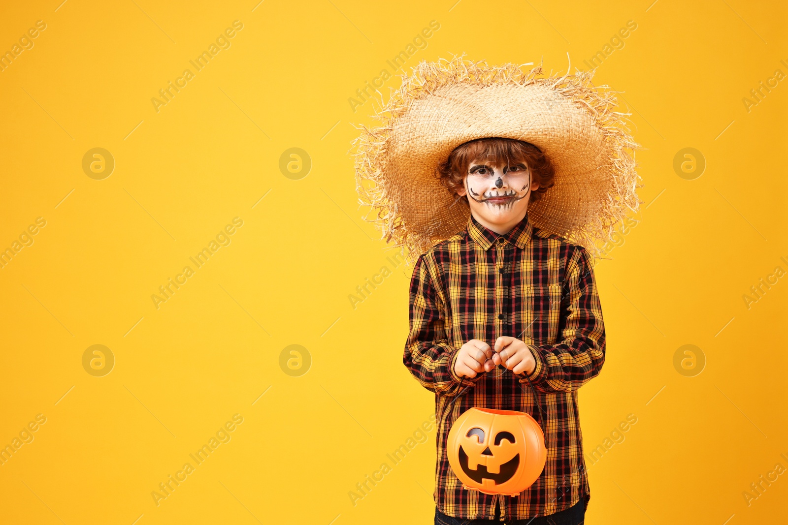 Photo of Funny boy with pumpkin bucket dressed like scarecrow on yellow background, space for text. Halloween celebration