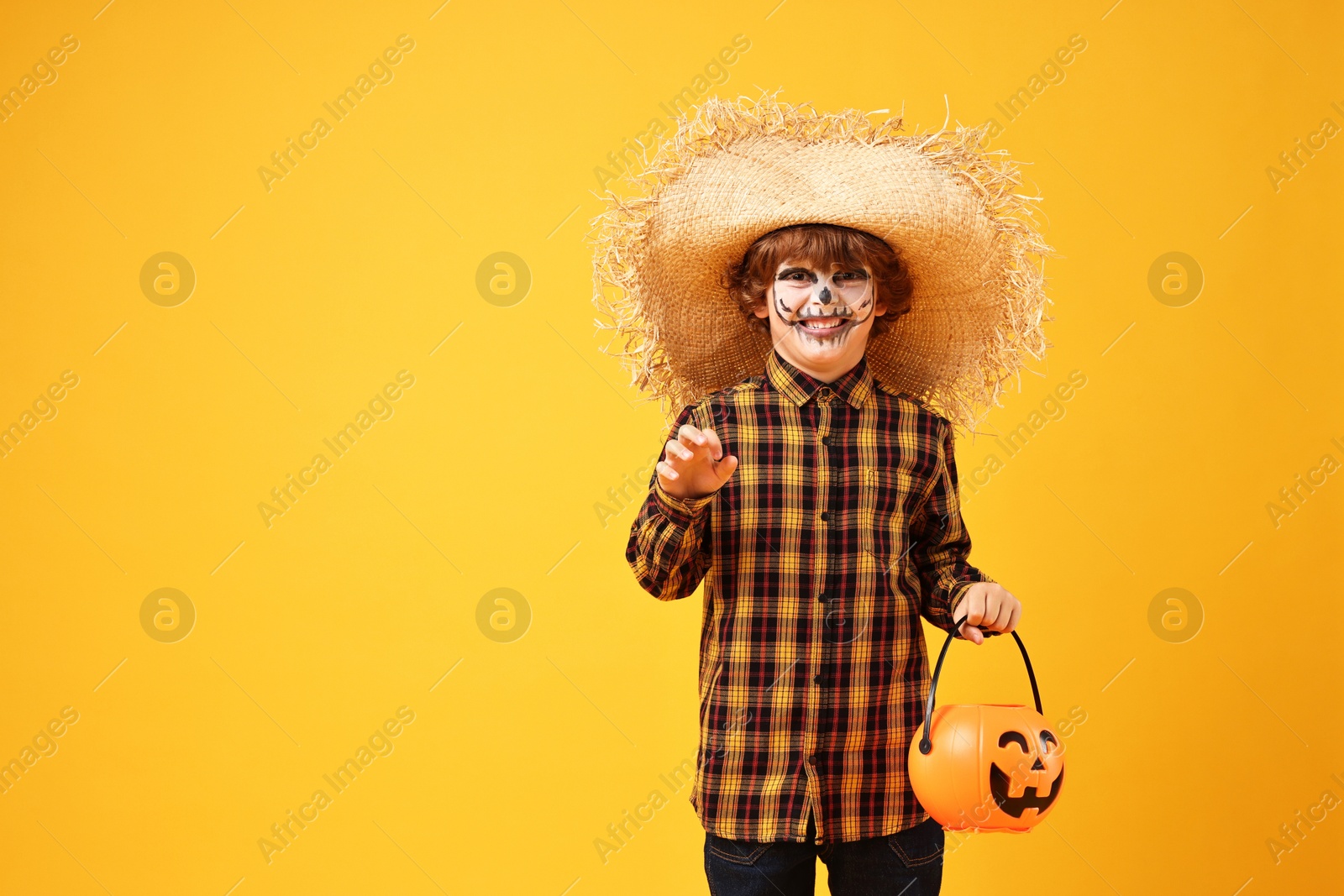 Photo of Funny boy with pumpkin bucket dressed like scarecrow on yellow background, space for text. Halloween celebration