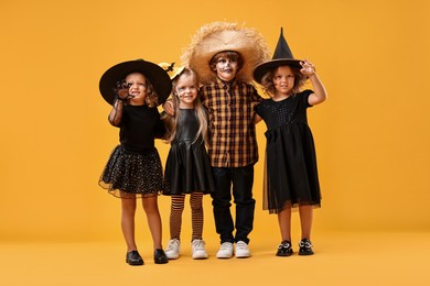 Photo of Cute children wearing Halloween costumes on orange background