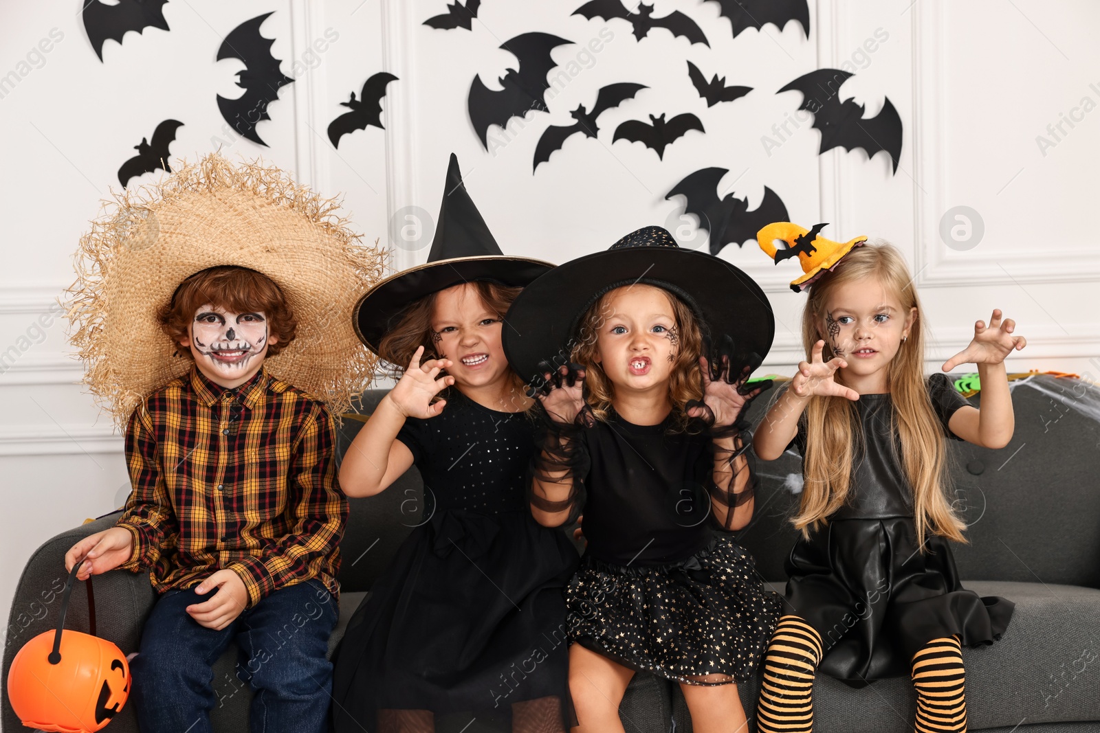 Photo of Cute children with pumpkin bucket wearing costumes indoors. Halloween celebration