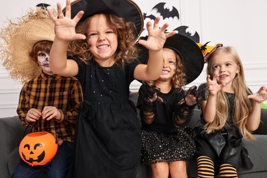 Photo of Cute children with pumpkin bucket wearing costumes indoors. Halloween celebration