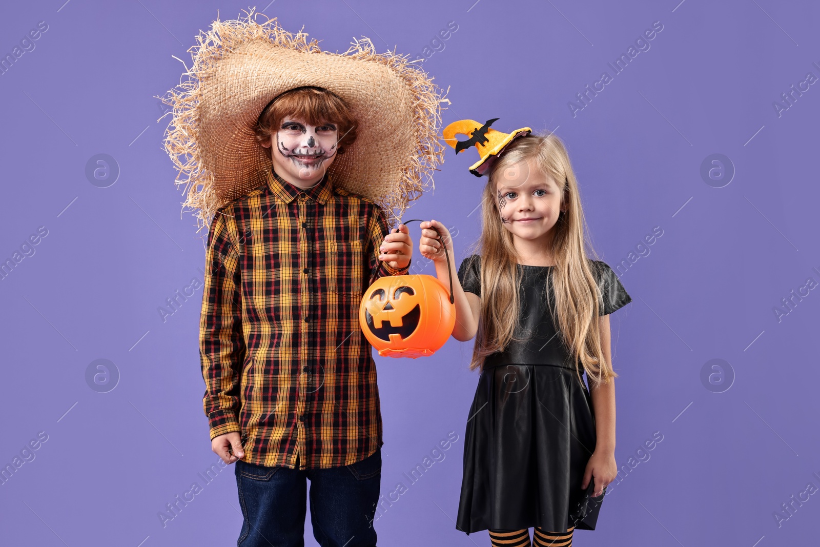 Photo of Cute children with pumpkin bucket wearing costumes on violet background. Halloween celebration