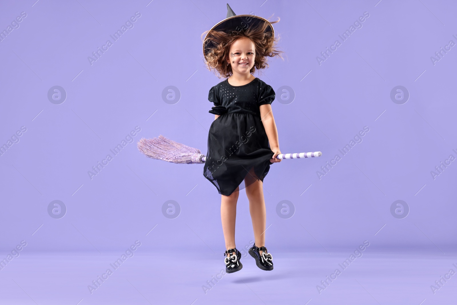 Photo of Funny girl with broom dressed like witch for Halloween celebration on violet background