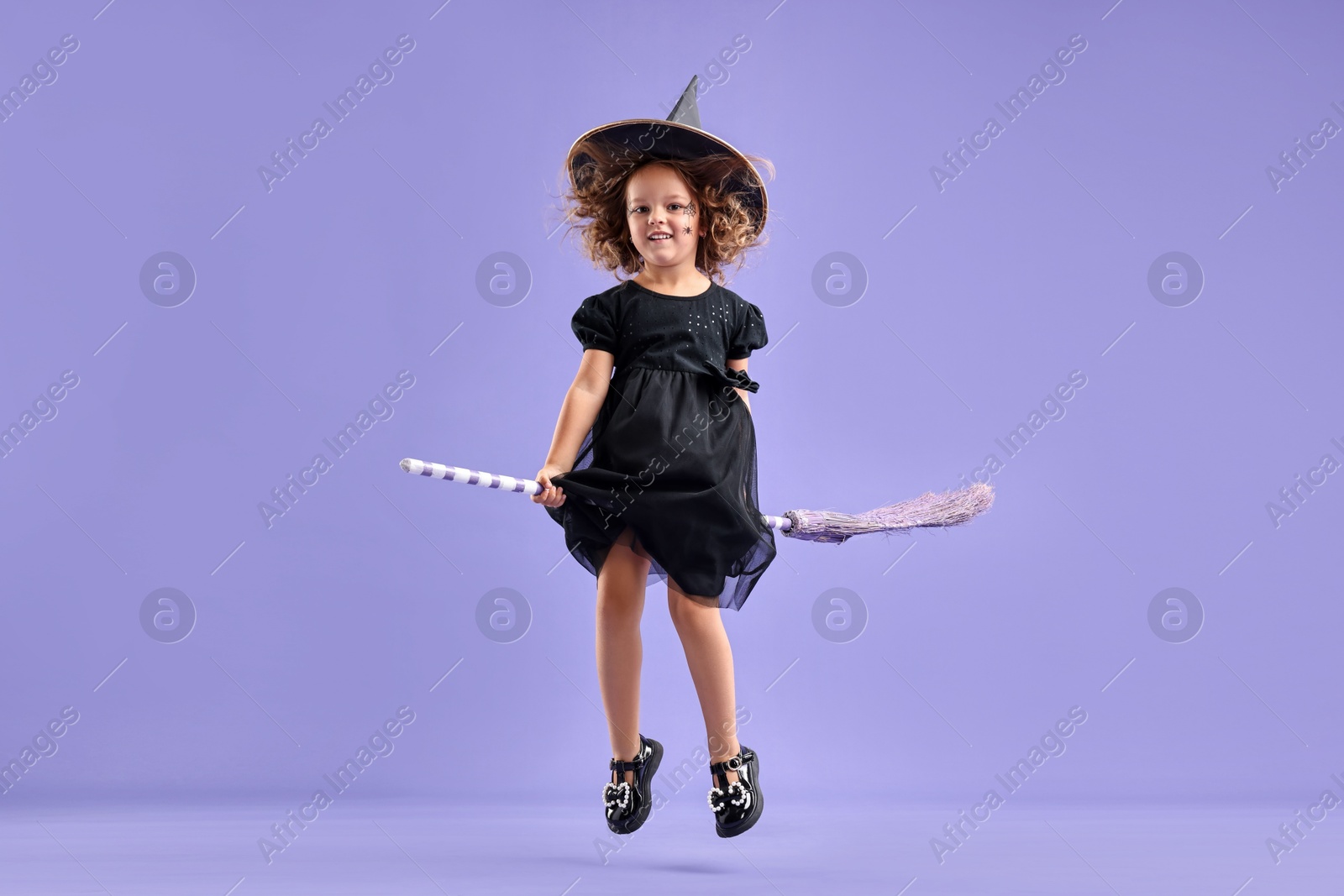 Photo of Funny girl with broom dressed like witch for Halloween celebration on violet background