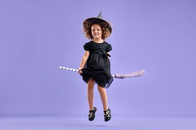 Photo of Funny girl with broom dressed like witch for Halloween celebration on violet background