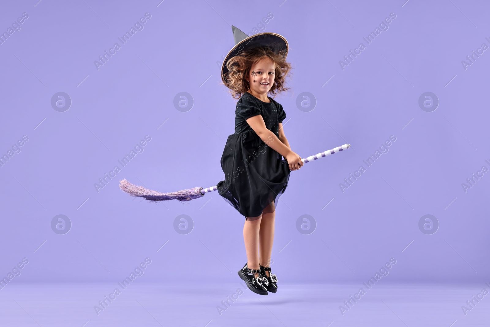 Photo of Funny girl with broom dressed like witch for Halloween celebration on violet background