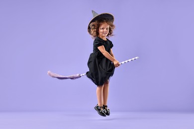 Photo of Funny girl with broom dressed like witch for Halloween celebration on violet background