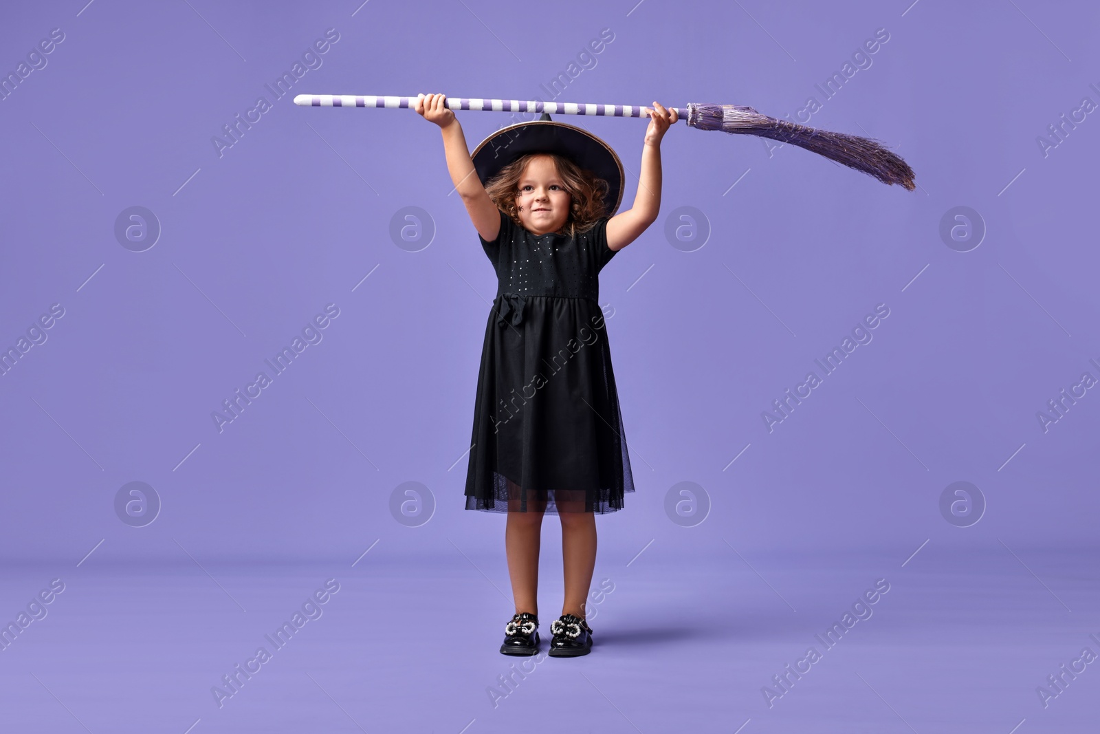 Photo of Funny girl with broom dressed like witch for Halloween celebration on violet background