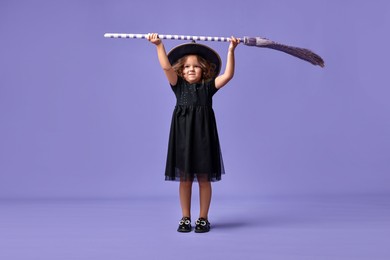 Funny girl with broom dressed like witch for Halloween celebration on violet background