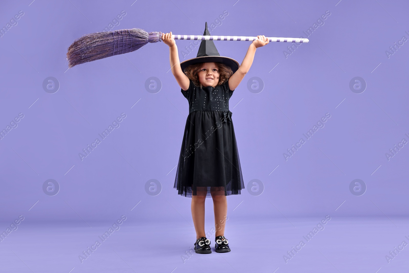 Photo of Funny girl with broom dressed like witch for Halloween celebration on violet background